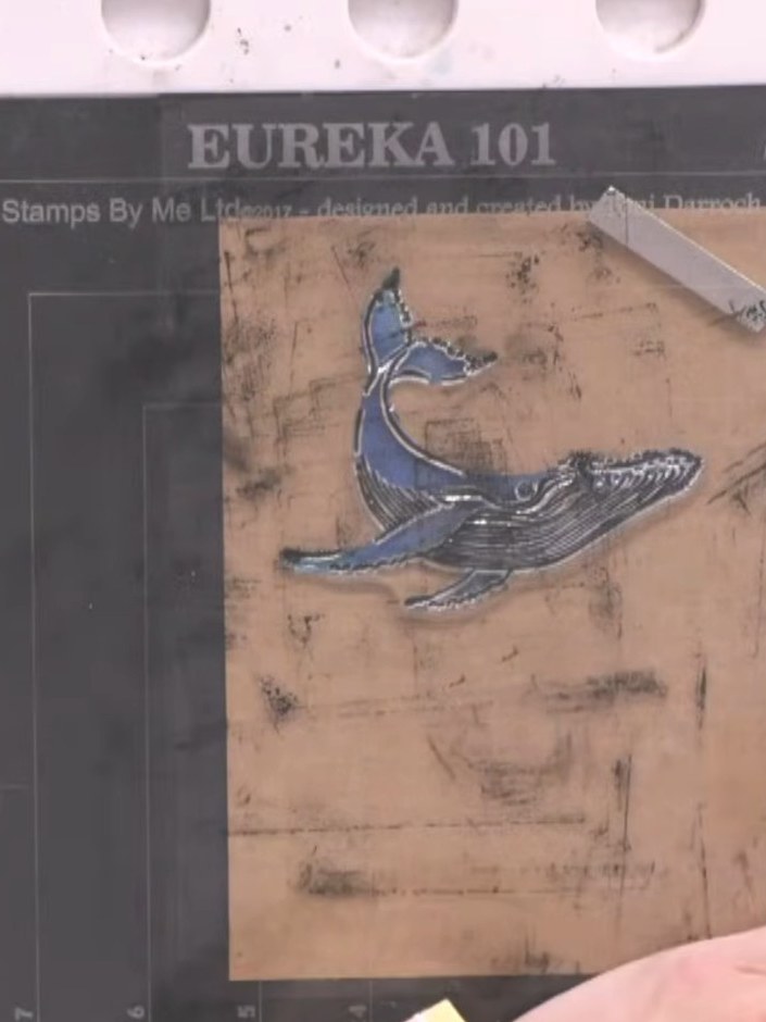 Step 8: Clean the whale stamp and re-ink the wave stamp with a different shade of blue ink. Spray the inked stamp with
