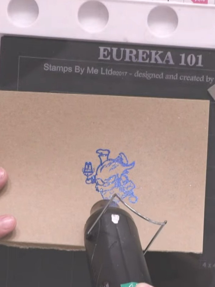 Step 4: Heat set the blue embossing powder on the stamped gnome image using a heat gun until the powder melts and beco