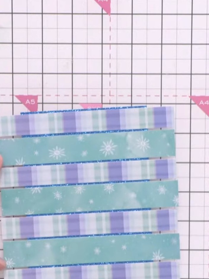 Step 7: Layer the alternating patterned paper strips horizontally across the blue glitter cardstock, creating a stripe