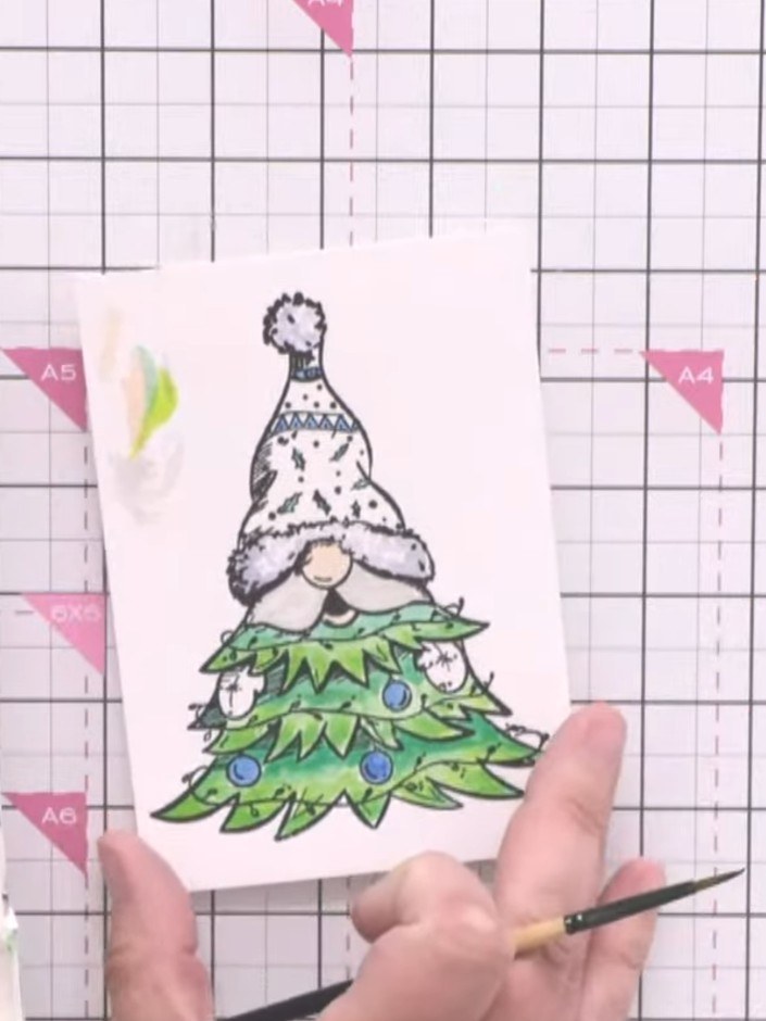 Step 2: Colour the gnome's hat with red watercolour paint. Use lighter green at the bottom of the Christmas tree and d
