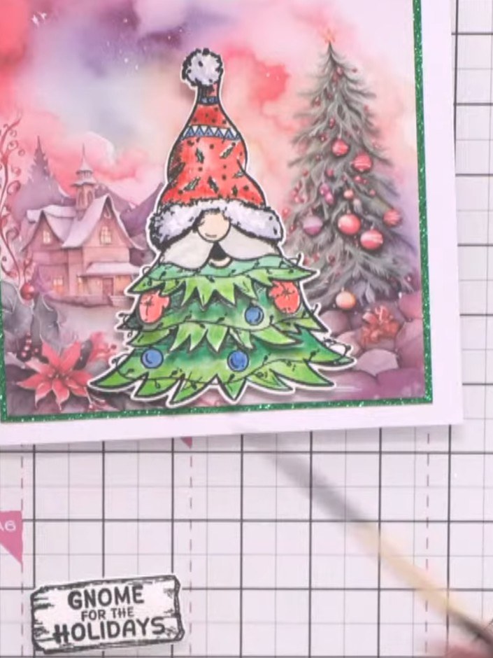 Step 8: Stamp the 'Gnome for the Holidays' sentiment onto white card stock and trim to create a small plaque. Brush th