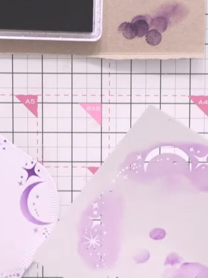 Step 5: Mount the patterned paper featuring purple celestial designs (moons and stars) onto the shaped card base. Posi