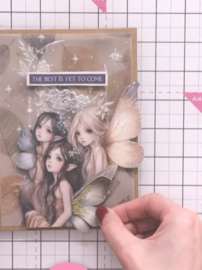 Step 11: Adhere the fairy figure flat to the card underneath the glitter-embellished wing, positioning it so the wings 