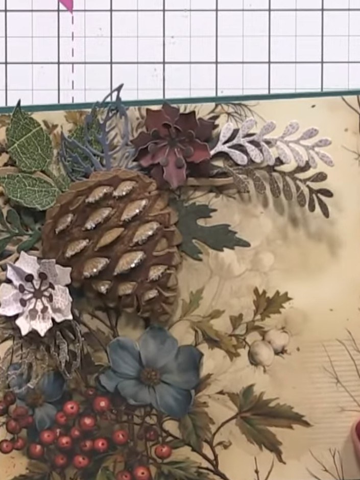 Step 9: Display the completed card with the layered pine cone, foliage, flowers and berries arrangement. The design fe