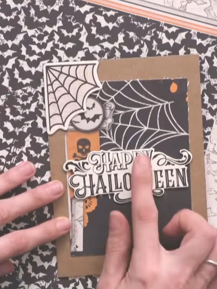 Step 7: Position and glue down the 'Happy Halloween' sentiment sticker in the centre of the black panel. Ensure all el