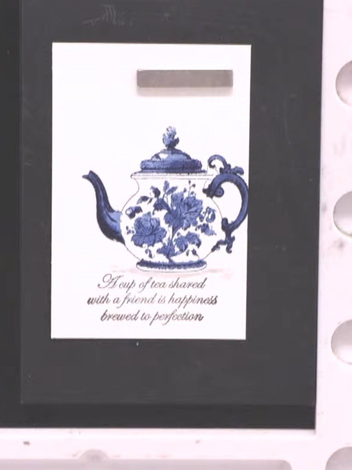 Step 10: Add a black ink sentiment stamp below the teapot image, positioning it centrally to complement the design. The