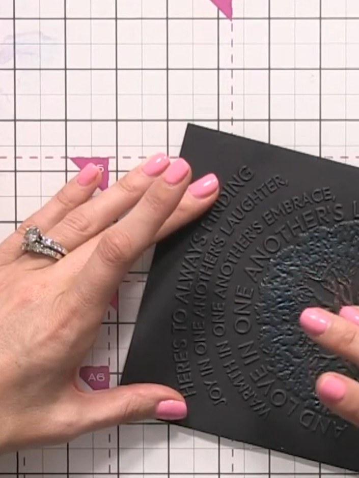 Step 6: Rub your finger over the embossed text and tree design on the black card to smooth and blend the metallic wax 