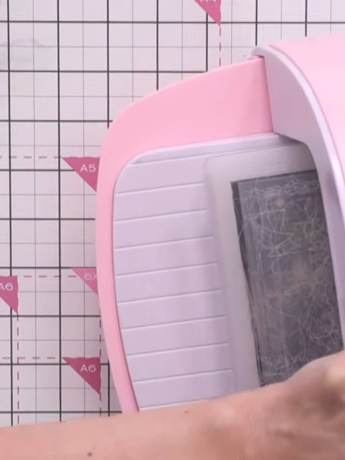 Step 3: Dreh das Papier durch deine Prägemaschine, damit das erhabene Motiv auf dem grauen Musterpapier entsteht.