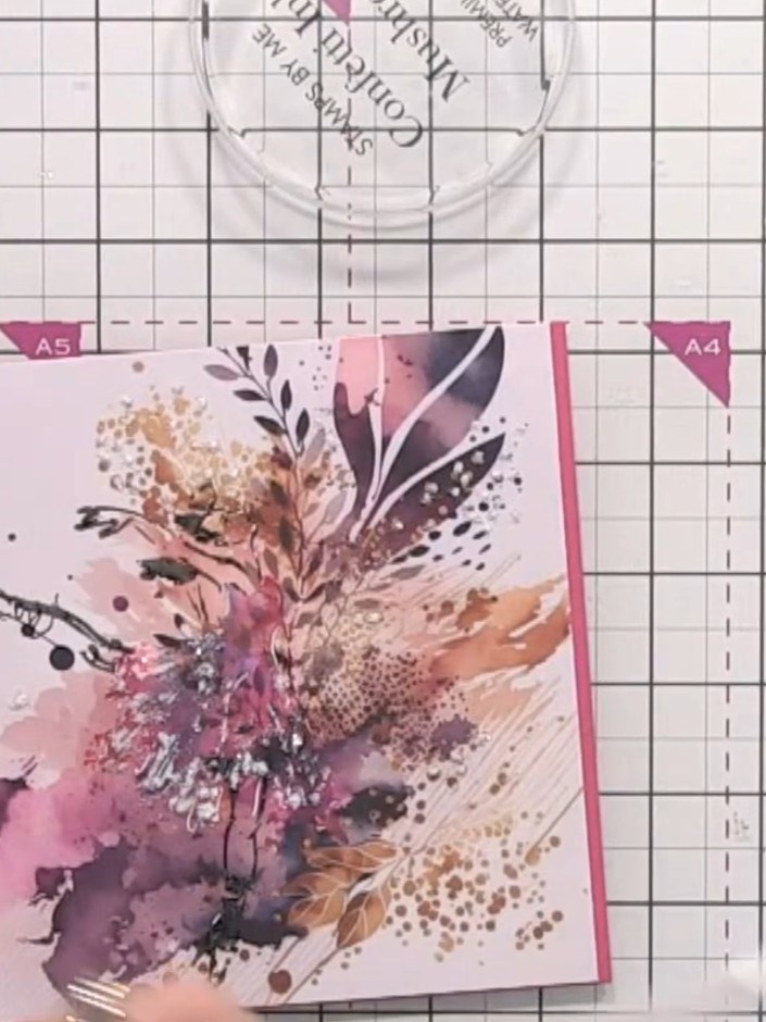 Step 10: Using a brush, add gold paint splats around the card, allowing the metallic gold to catch the light alongside 