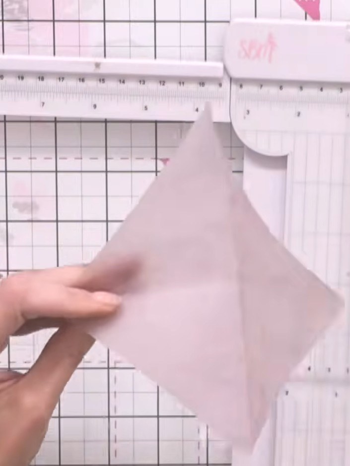 Step 2: Fold the vellum square diagonally from corner to corner. Then fold the opposite corners in towards the centre 