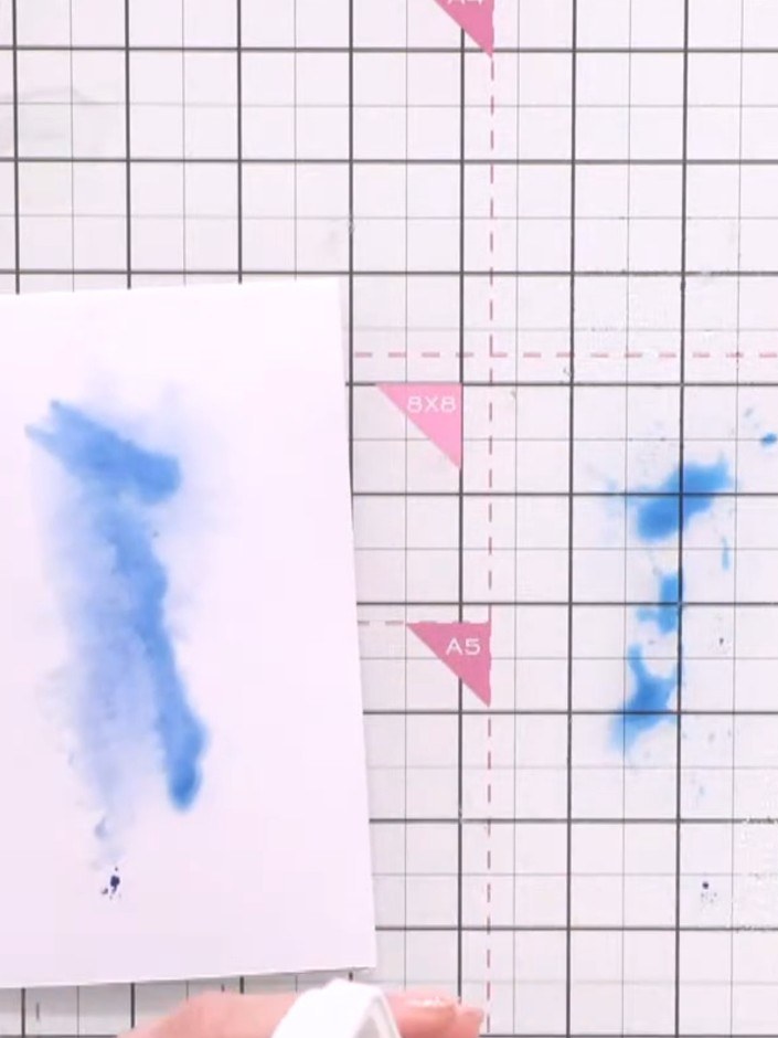Step 1: Spray blue ink onto your craft mat with water to create a watercolour wash. Place your white cardstock onto th