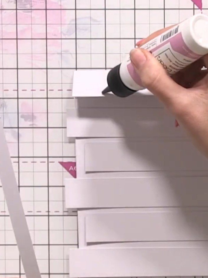 Step 5: Apply glue along a long strip of white card and place it horizontally across the back of all the vertical stri