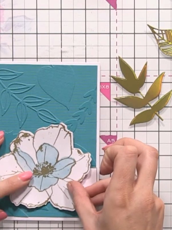 Step 15: Position the gold heat-embossed flower and foliage pieces onto the teal embossed card front. Arrange them to a
