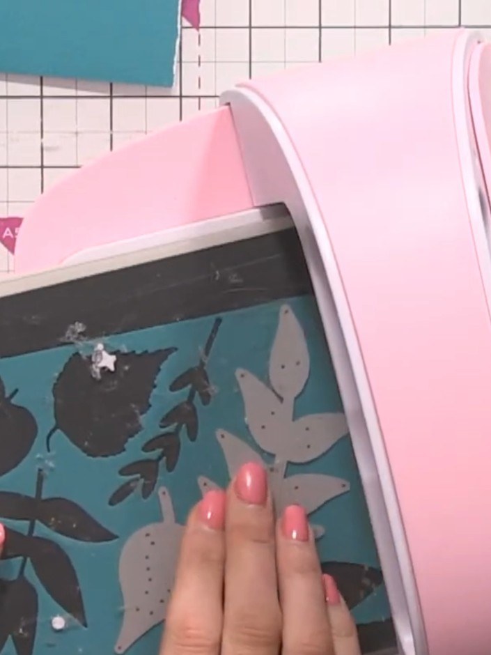 Step 4: Place your teal card panel with the die-cut floral design on top into the pink die-cutting machine. Run the la