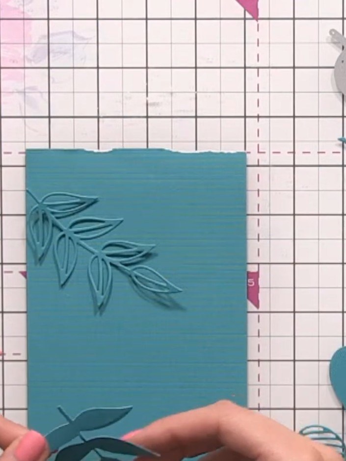 Step 6: Glue the die-cut leaf pieces randomly onto the second sheet of teal card to create dimension. Position them at