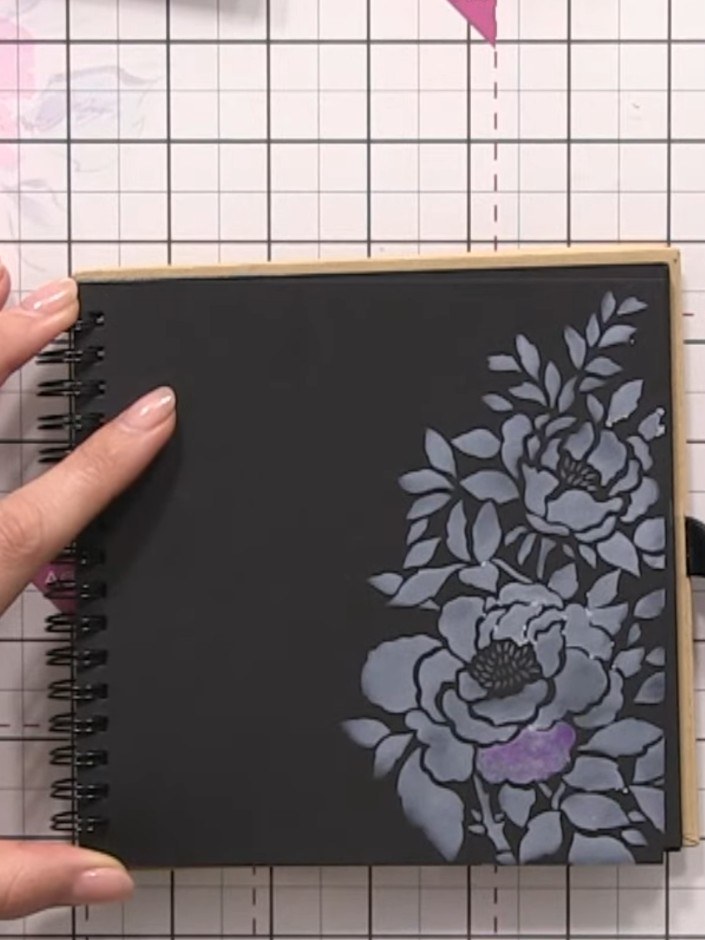Step 4: Using a damp brush, paint the diluted purple ink over the white stencilled floral design on the black card. Al