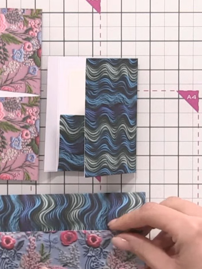 Step 2: Score and fold the blue wave patterned paper to create a base pocket. Position the folded pocket on your work 