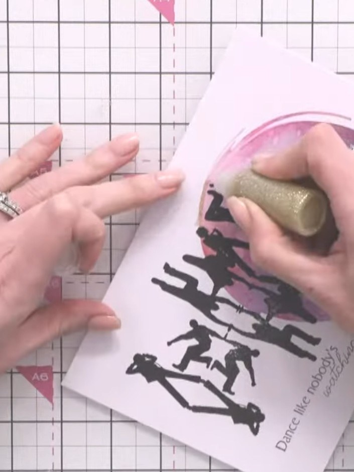 Step 13: Optional: Apply gold glitter glue in a halo around the stamped dancers, avoiding the black ink. This adds a su