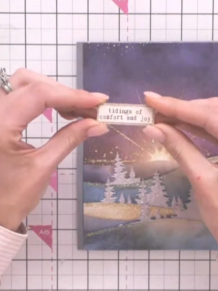 Step 9: Cut out a pre-printed sentiment reading 'Tidings of Comfort and Joy' and adhere it to the card front below the