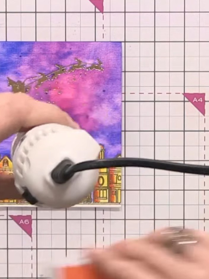 Step 9: Dry the card completely using a heat gun, moving it steadily over the watercoloured sky and buildings until fu