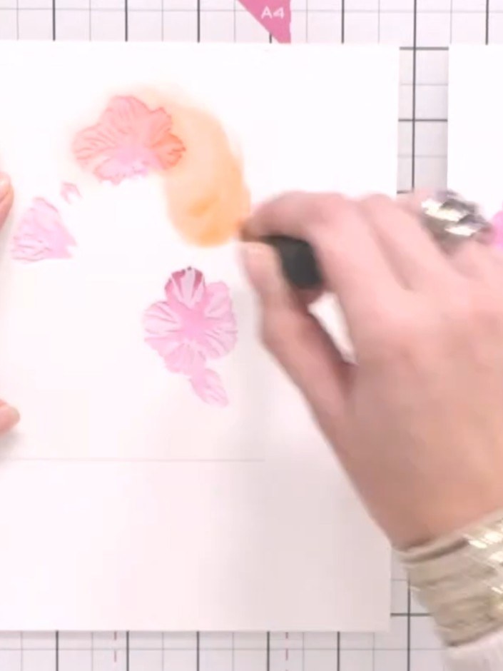 Step 7: Remove the first stencil and position the second hibiscus stencil on your watercolour card. Apply orange ink t
