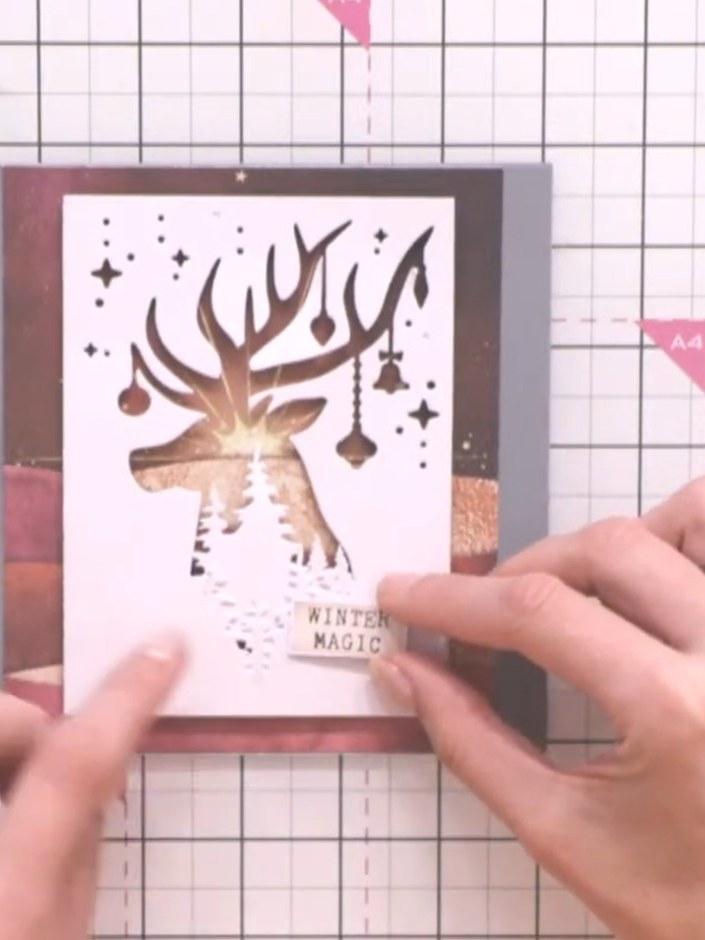 Step 11: Apply a pre-printed sentiment reading 'WINTER MAGIC' from the kit to the lower portion of the card front, posi