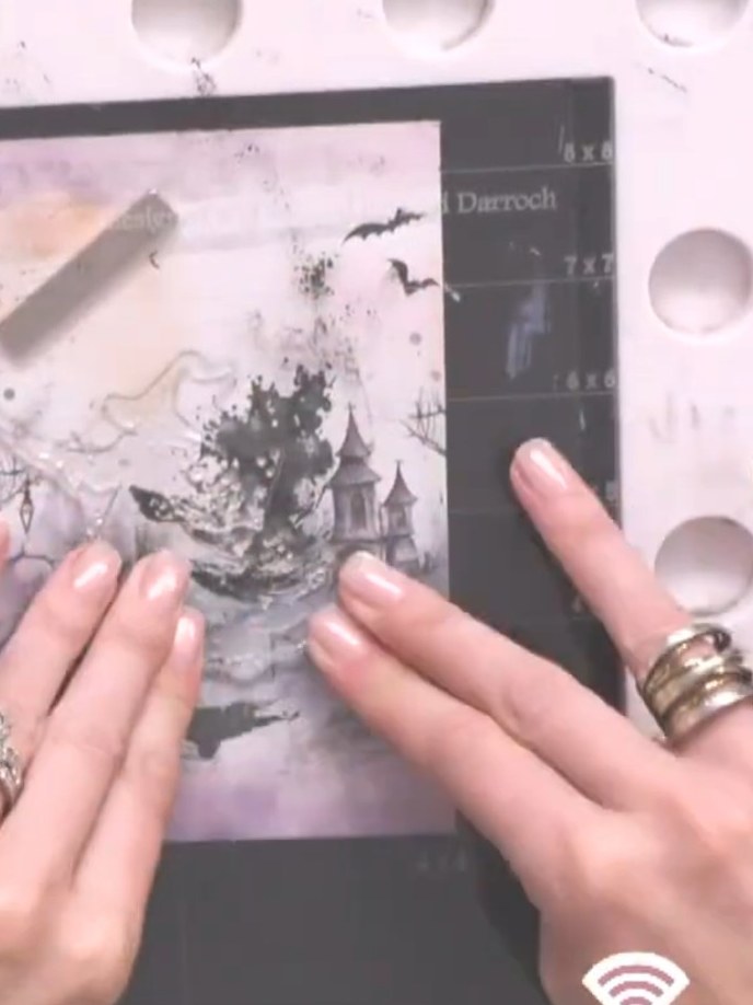 Step 8: Position the detailed witch stamp carefully over the dried watercolour background, using the packet image as a