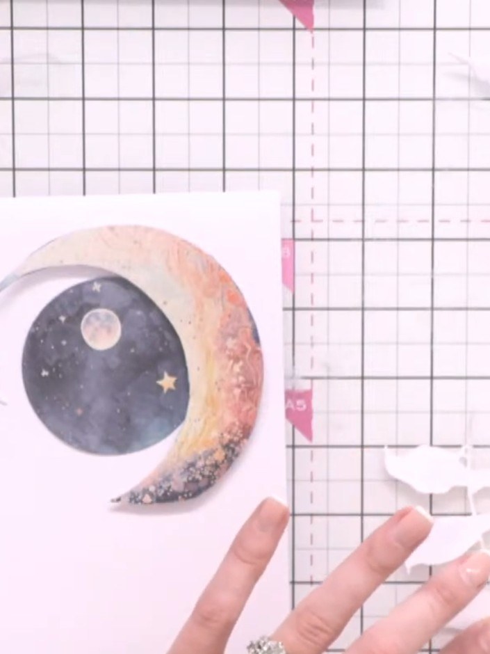 Step 8: Attach the fussy-cut moon flat to the card base using adhesive tape, positioning it centrally on the card fron