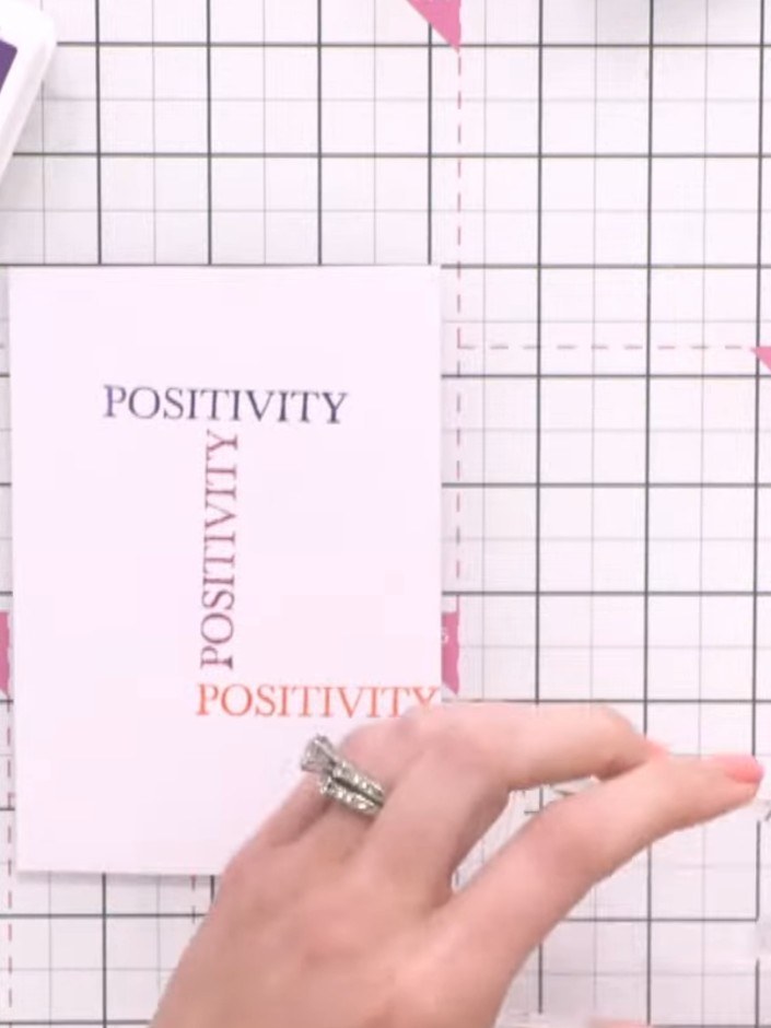 Step 6: Stamp the word 'positivity' a third time onto the card panel using another colour ink to continue building up 