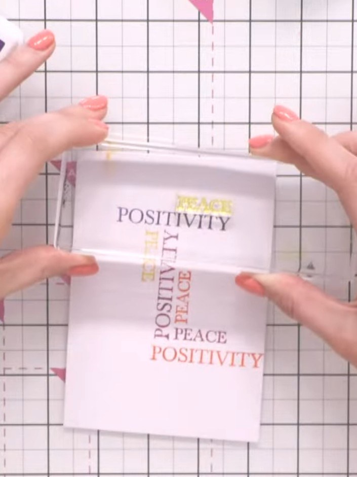 Step 8: Stamp the word 'peace' multiple times across the white card background in different colours from your ink pads