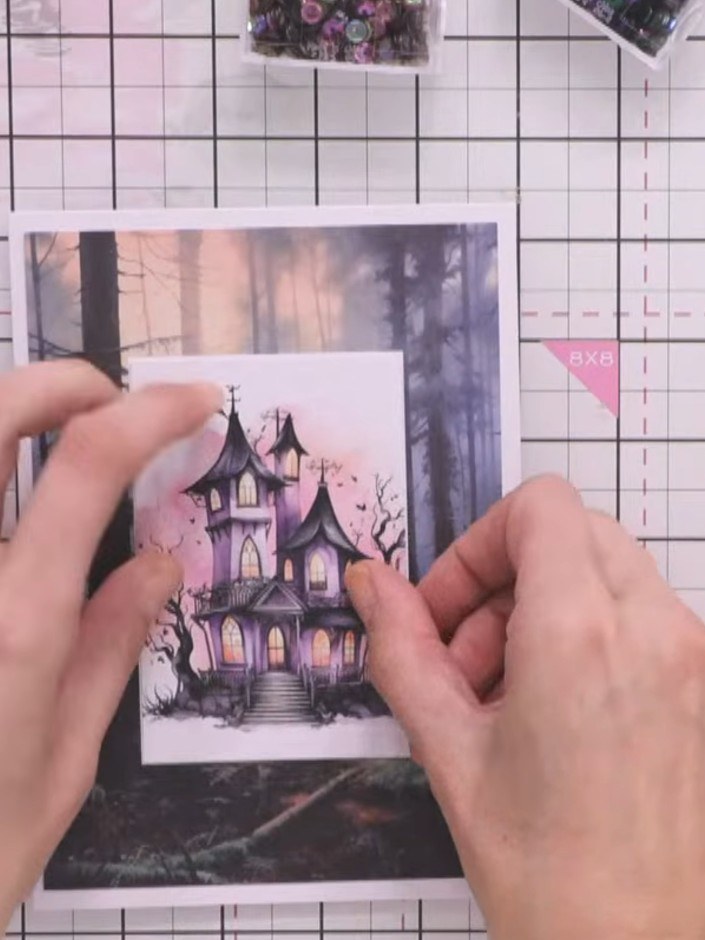 Step 11: Apply foam pads to the back of the fussy-cut haunted house and character pieces. Position them inside the fram