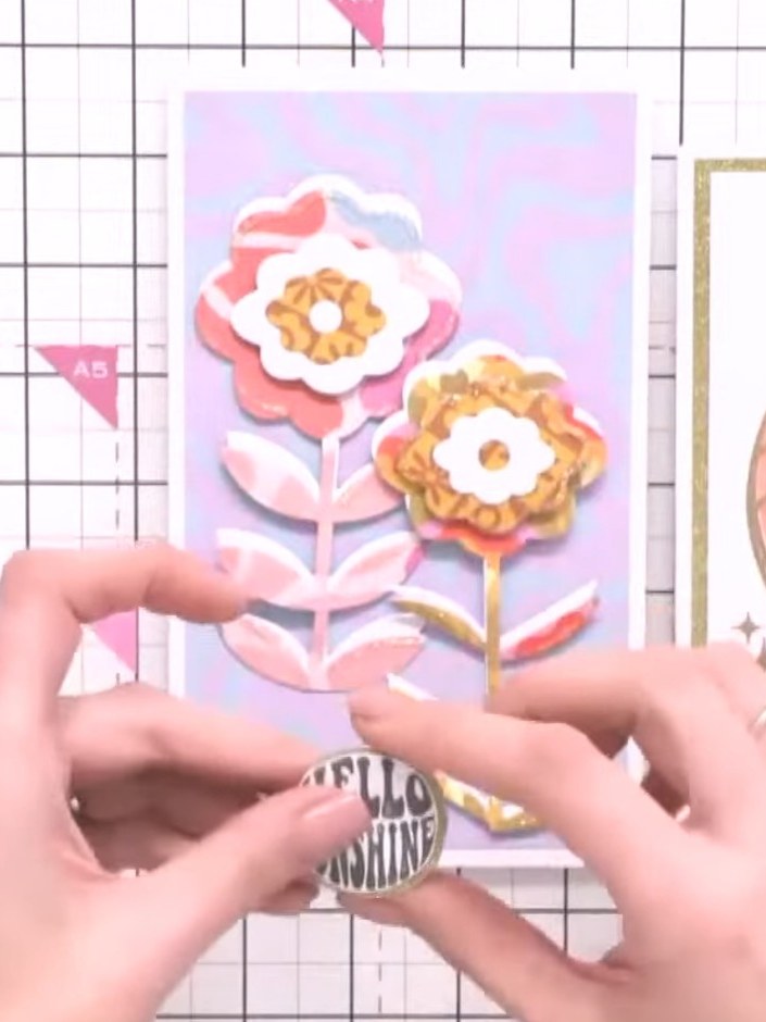 Step 7: Add a 'Hello Sunshine' sentiment badge and decorative flowers to your card. Position silhouette figures of dan