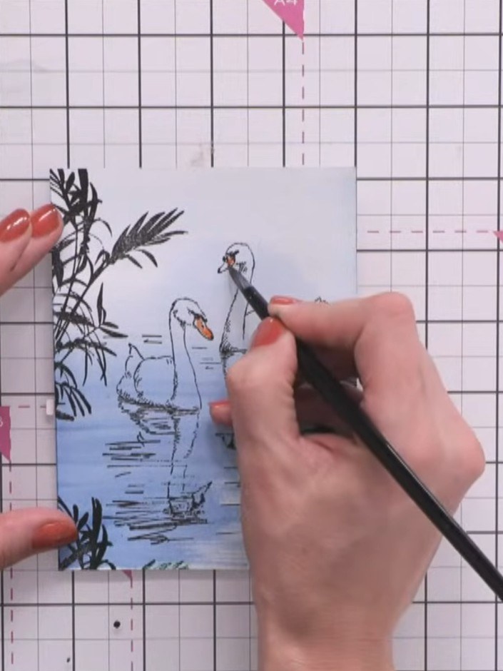 Step 8: Use the orange ink pad to add colour to the swans' beaks. Add a hint of orange to the reflection below each be