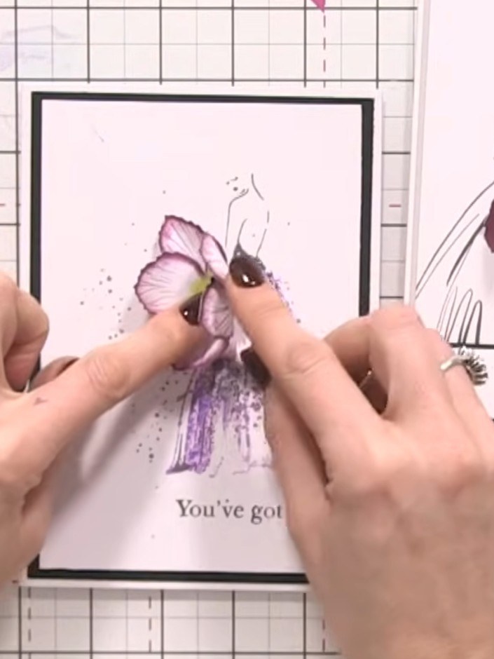 Step 10: Position the completed purple flower onto the card front, placing it so it appears to be held by or emerging f