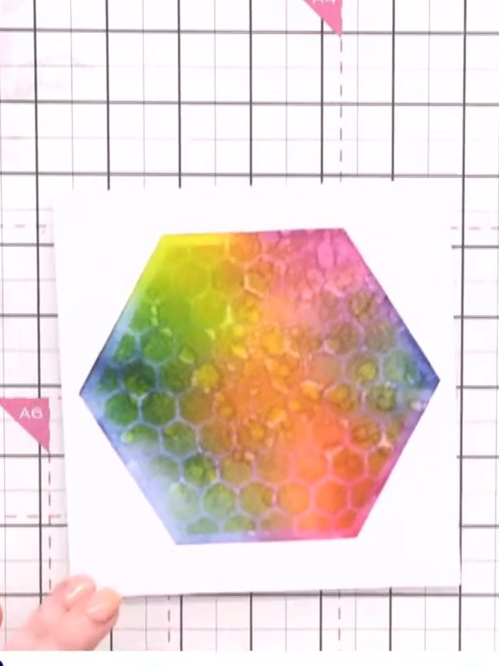 Step 10: Carefully remove the honeycomb stencil from the card to reveal the rainbow coloured textured background. Allow