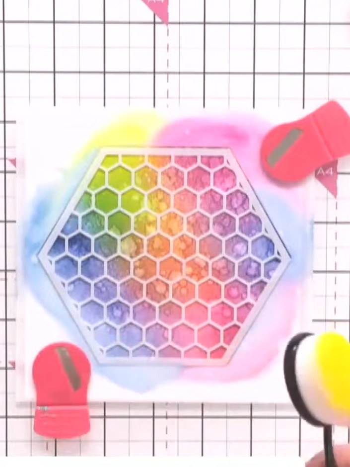 Step 9: Reposition the honeycomb stencil over your rainbow background. Use a blending tool to apply yellow ink through