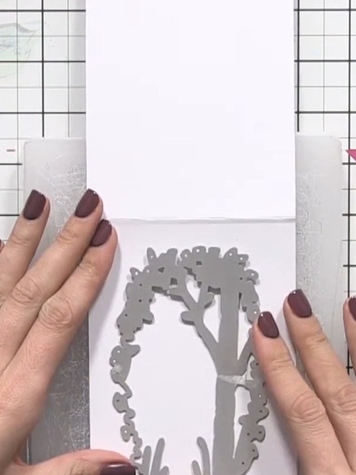 Step 1: Open your card base and position the floral wreath aperture die onto a piece of white card stock. Smooth it do