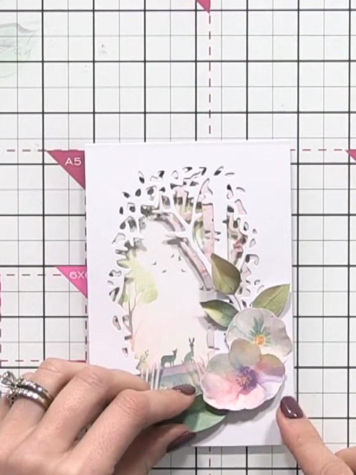 Step 11: Adhere the flower cluster to the card front, positioning it within the aperture window. The floral elements sh