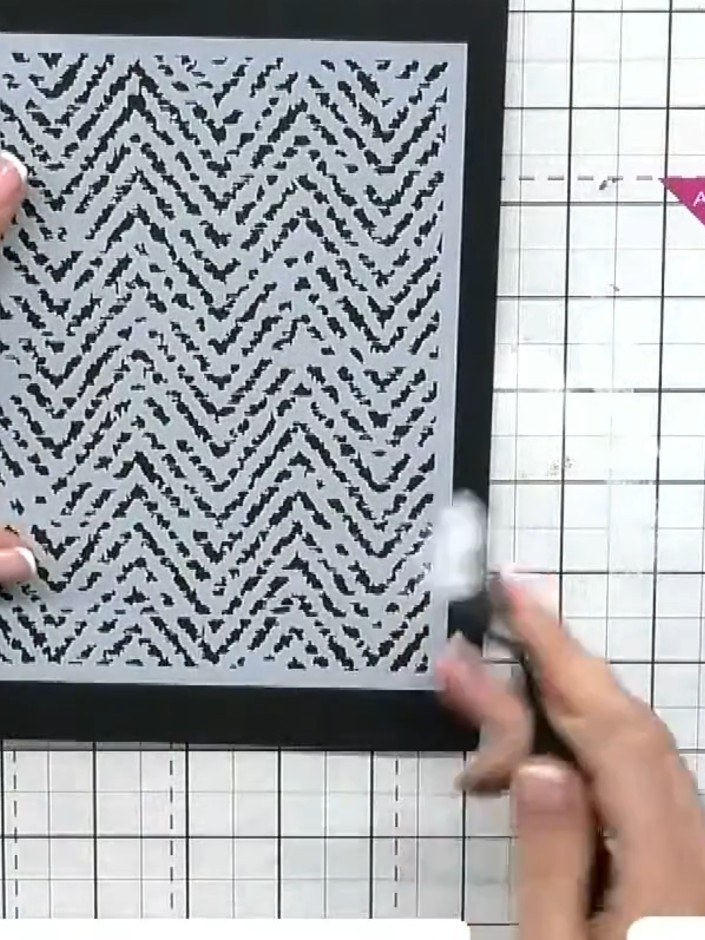 Step 1: Prepare a black card base. Position the Herringbone stencil centrally on top of the card base, holding it in p