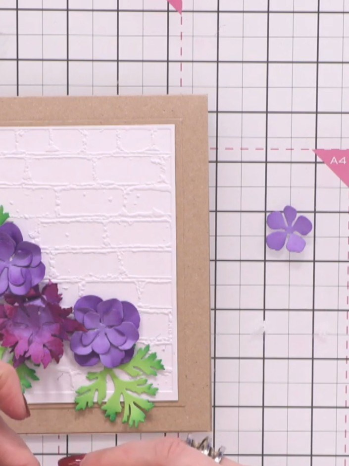 Step 13: Position your green leaves underneath and around the purple flowers to fill gaps and create a natural arrangem