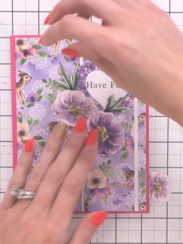 Step 11: Position and adhere the fussy-cut purple flowers around the heart sentiment in a balanced formation. Layer the