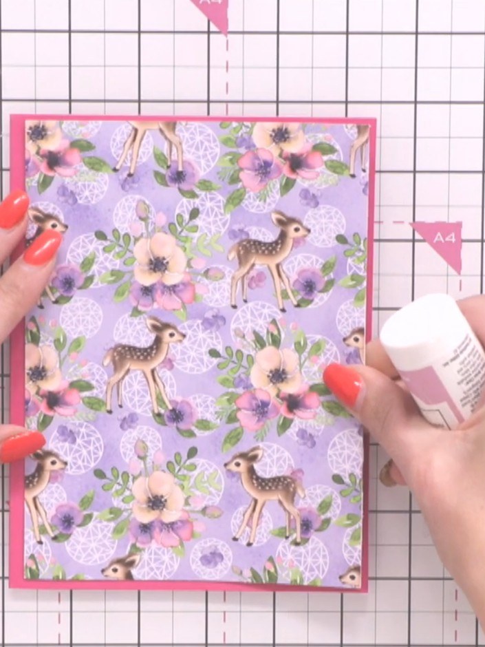 Step 5: Schneide ein Stück vom lila geblümten Musterpapier zu und klebe es mit Kleber auf den rosa Kartenrohling.