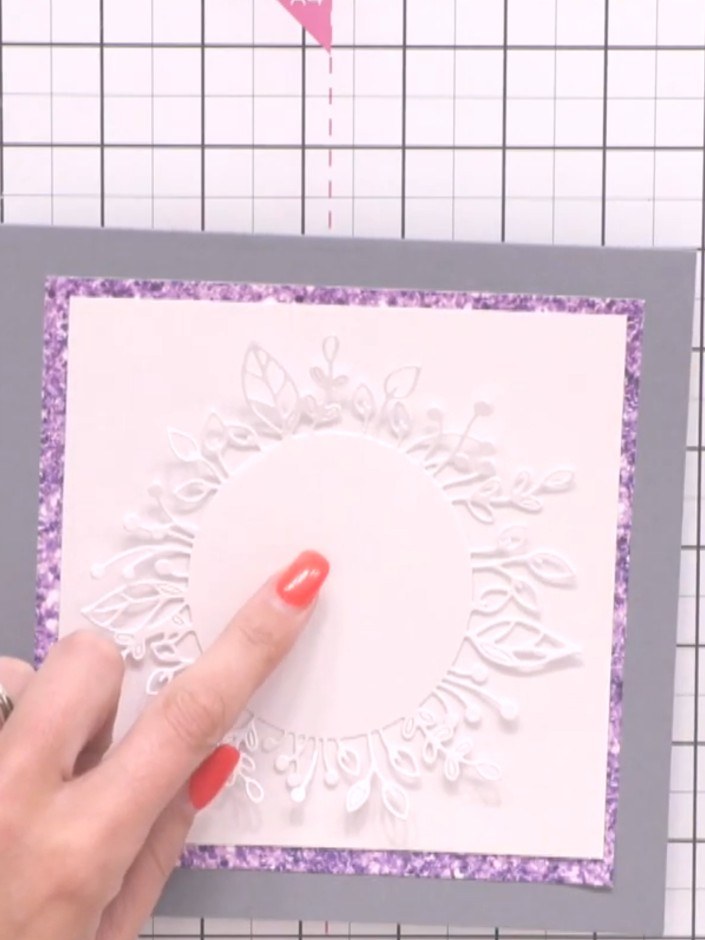 Step 6: Position the white embossed wreath die-cut centrally on the card front and glue it in place. Press down firmly