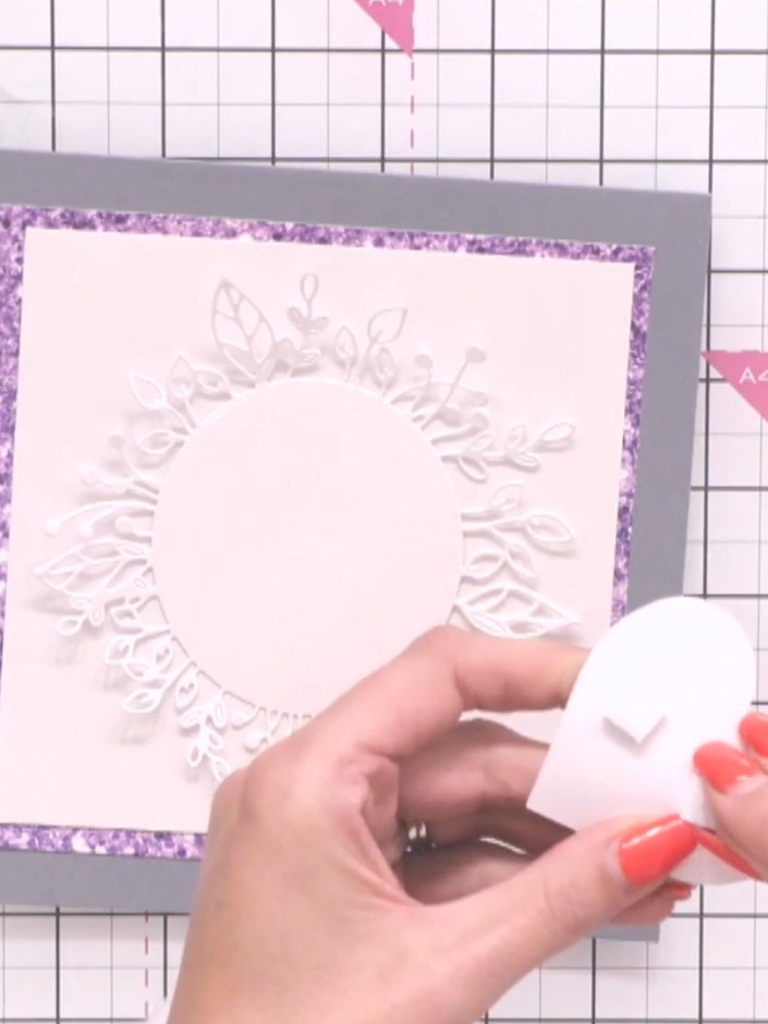 Step 7: Apply adhesive pads to the back of the white cascading hearts embellishment. Attach it to the centre of the em