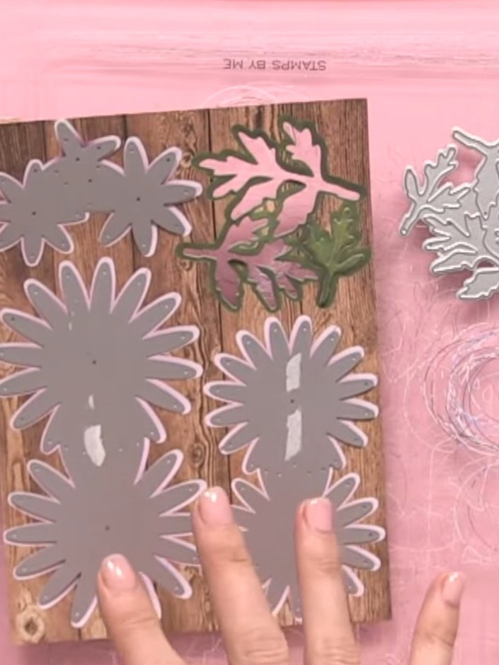 Step 9: Position the green foliage pieces between and around the grey chrysanthemum flowers on the wood-effect panel. 