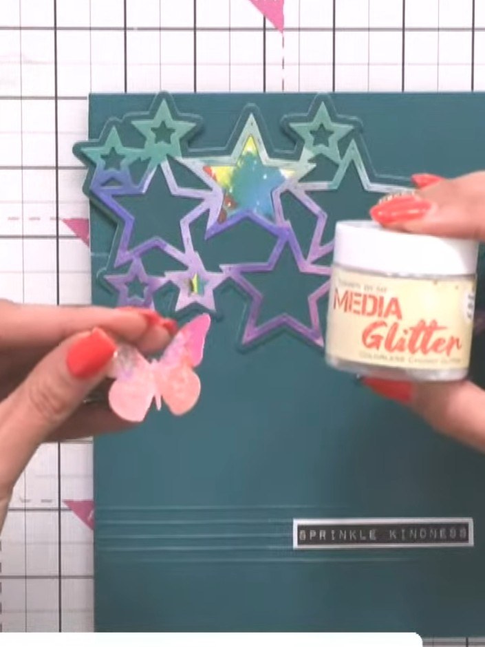 Step 9: Add media glitter to the butterfly elements for extra sparkle. Apply the colourless chunky glitter to give a g