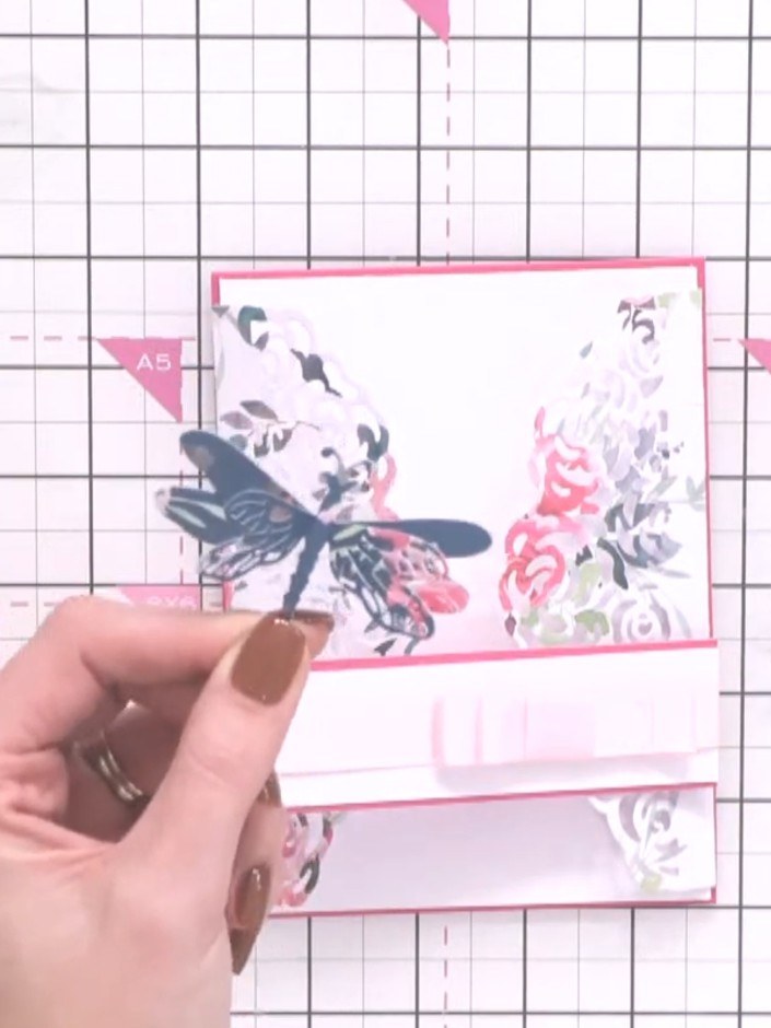 Step 9: Layer the dragonfly die-cuts onto the card, positioning them above the ribbon bow. Stack the teal base layer, 