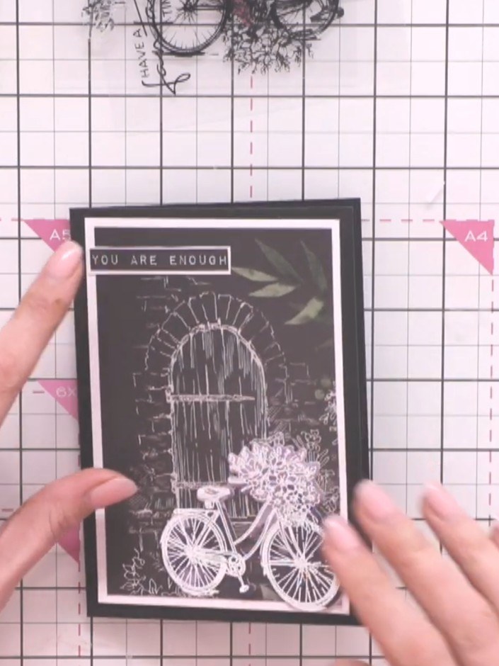 Step 12: Trim a sentiment strip reading 'YOU ARE ENOUGH' from the paper pad. Adhere it to the top of the card front to 