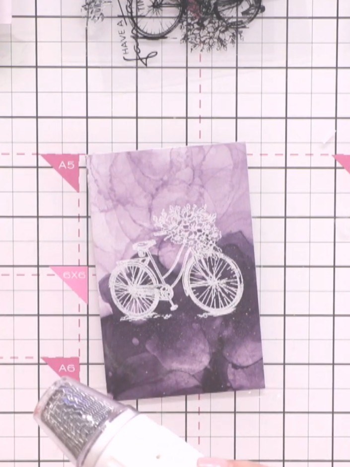 Step 6: Heat the embossing powder with a heat gun until it melts and sets, creating a raised gold finish on the bicycl