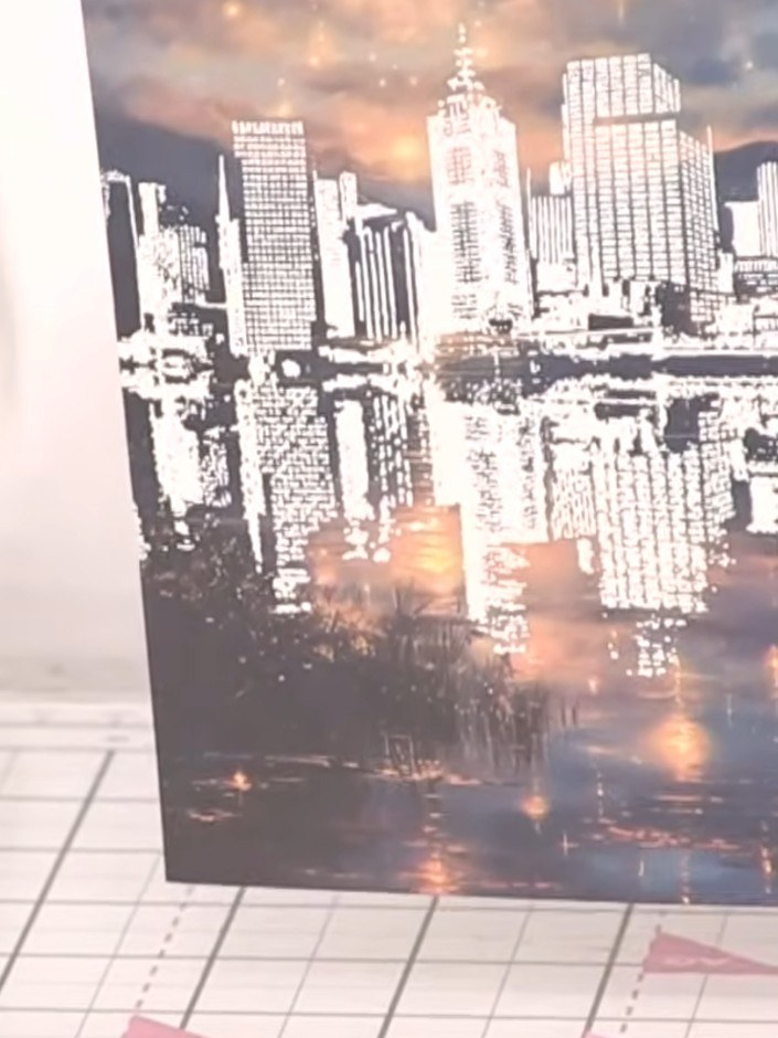 Step 8: Mount the trimmed cityscape piece onto a white card blank, positioning it to showcase the embossed fireworks a